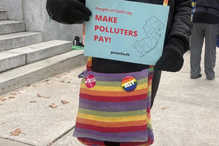 a sign reads People of Faith say MAKE POLLUTERS PAY!