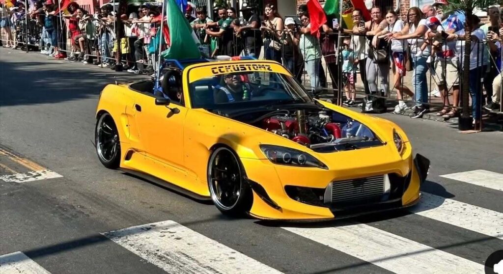 A bright yellow sports car drives slowly down the street during the parade.