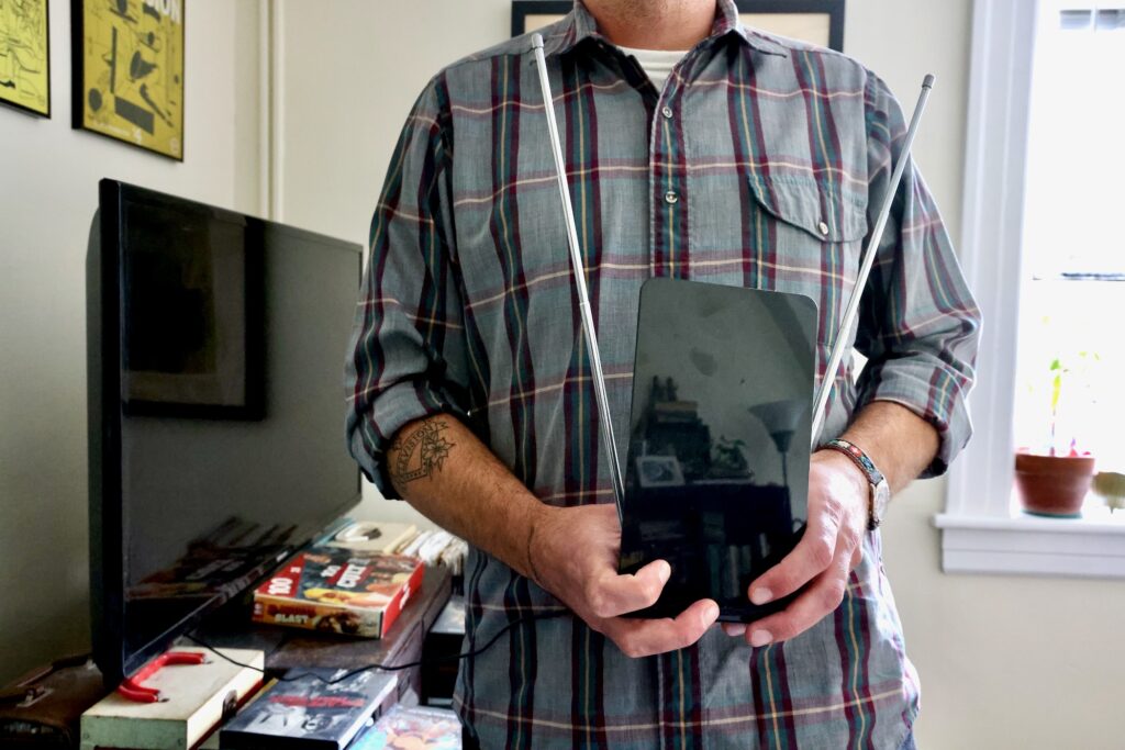 James Heimer is in his home, holding up the TV antenna he uses.