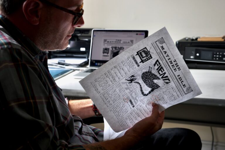 James Heimer is sitting at his desk, examining an issue of his print newsletter, 'The Matinee Idle.'