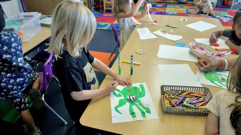 2026 10 16-e lee-philadelphia settlement music school-kaleidoscope preschool drawing A group of children are sitting at a table drawing. One child is coloring in a green monster.