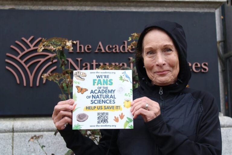 a woman holds a sign reading WE'RE FANS OF THE ACADEMY OF NATURAL SCIENCES HELP US SAVE IT!
