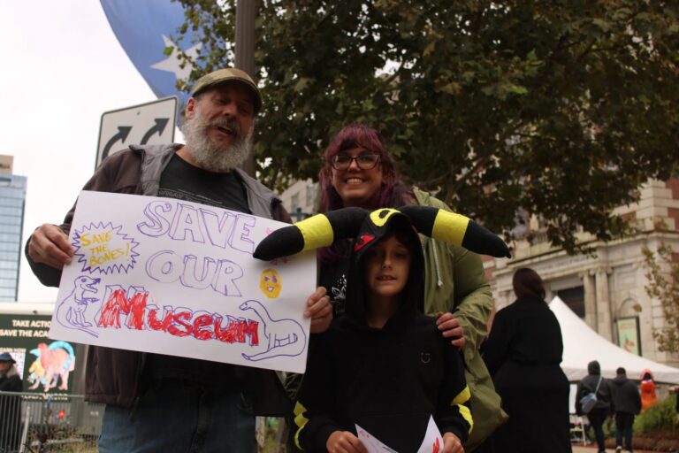 two adults and a child at the rally, one adult holding a sign reading SAVE OUR MUSEUM