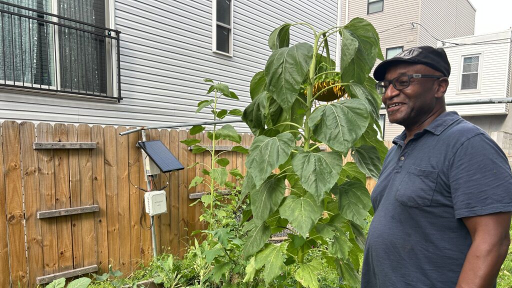air-quality-monitoring-west-philadelphia-2026-ss-11-cropped An air quality monitor stands among flowers and vegetables in a garden with Greg Jenkins