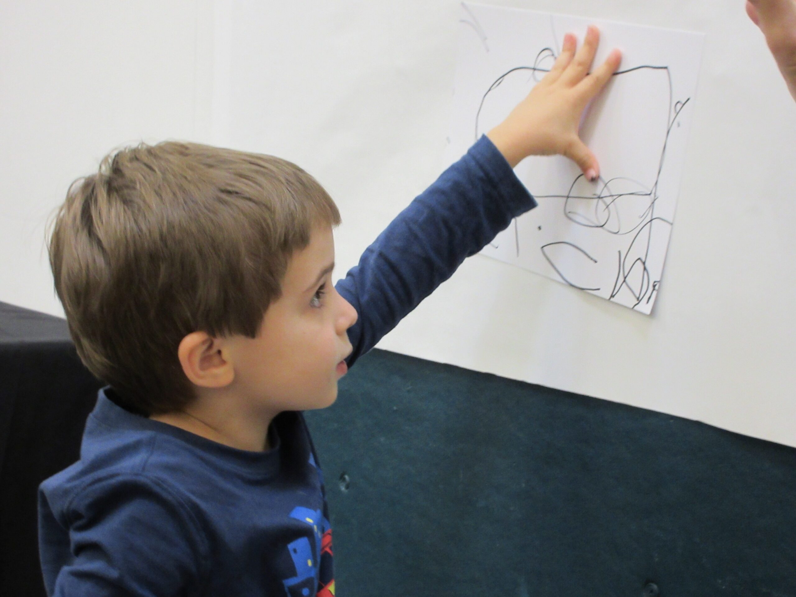 A child puts their drawing on a wall