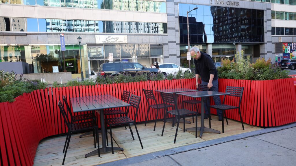 three tables with chairs in the street off the sidewalk by LOVE Park