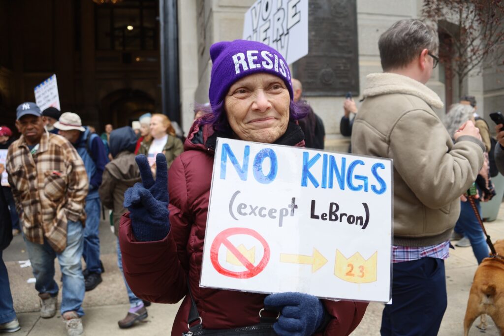 no-kings-philadelphia-rrastegari-2026-10-17-05 Wendy Foreman, dressed in a winter coat and hat which says 'RESIST' is holding up a sign that says 'No Kings (except Lebron)' outside of Philadelphia City Hall for the No Kings protest.