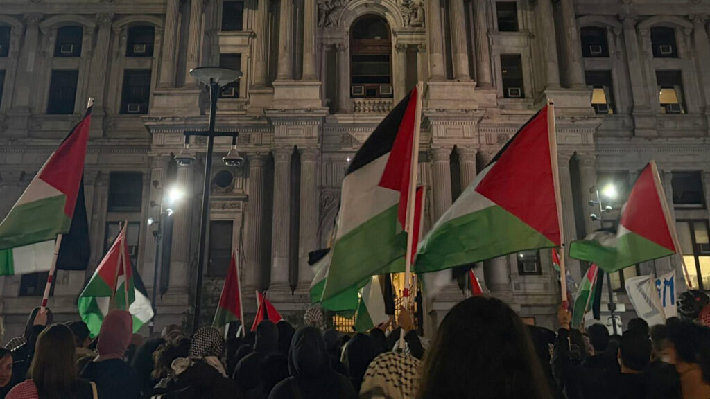 rittenhouse-israel-protest-amcgurl-2026-10-08-8-scaled-cropped A large group of protesters waving Palestinian flags stand in front of Philadelphia City Hall at night.